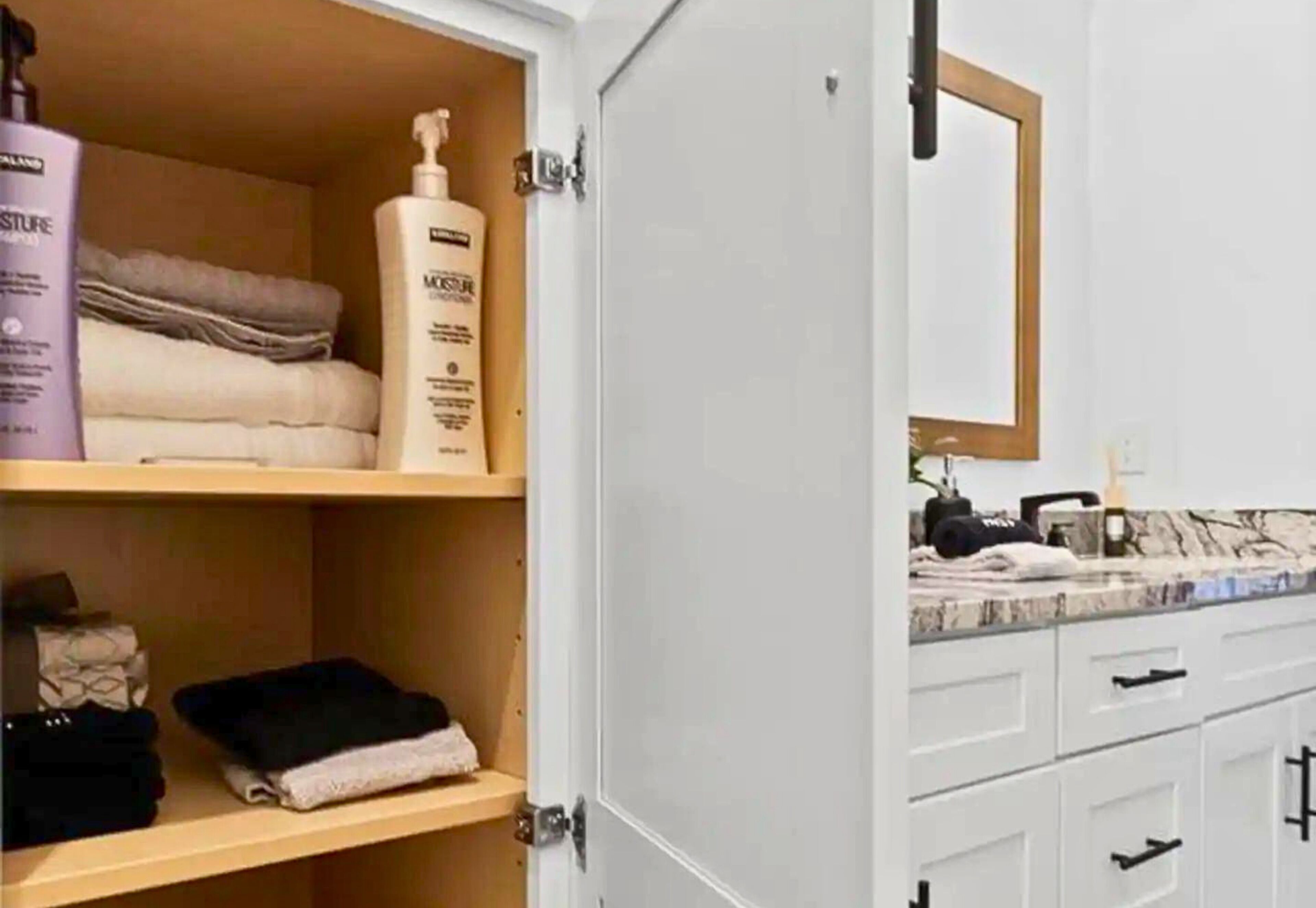 A bathroom with a white vanity, a mirror, and shelves with toiletries.