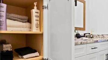 A bathroom with a white vanity, a mirror, and shelves with toiletries.
