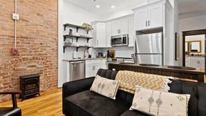 A modern kitchen with white cabinets, stainless steel appliances, and a brick wall.