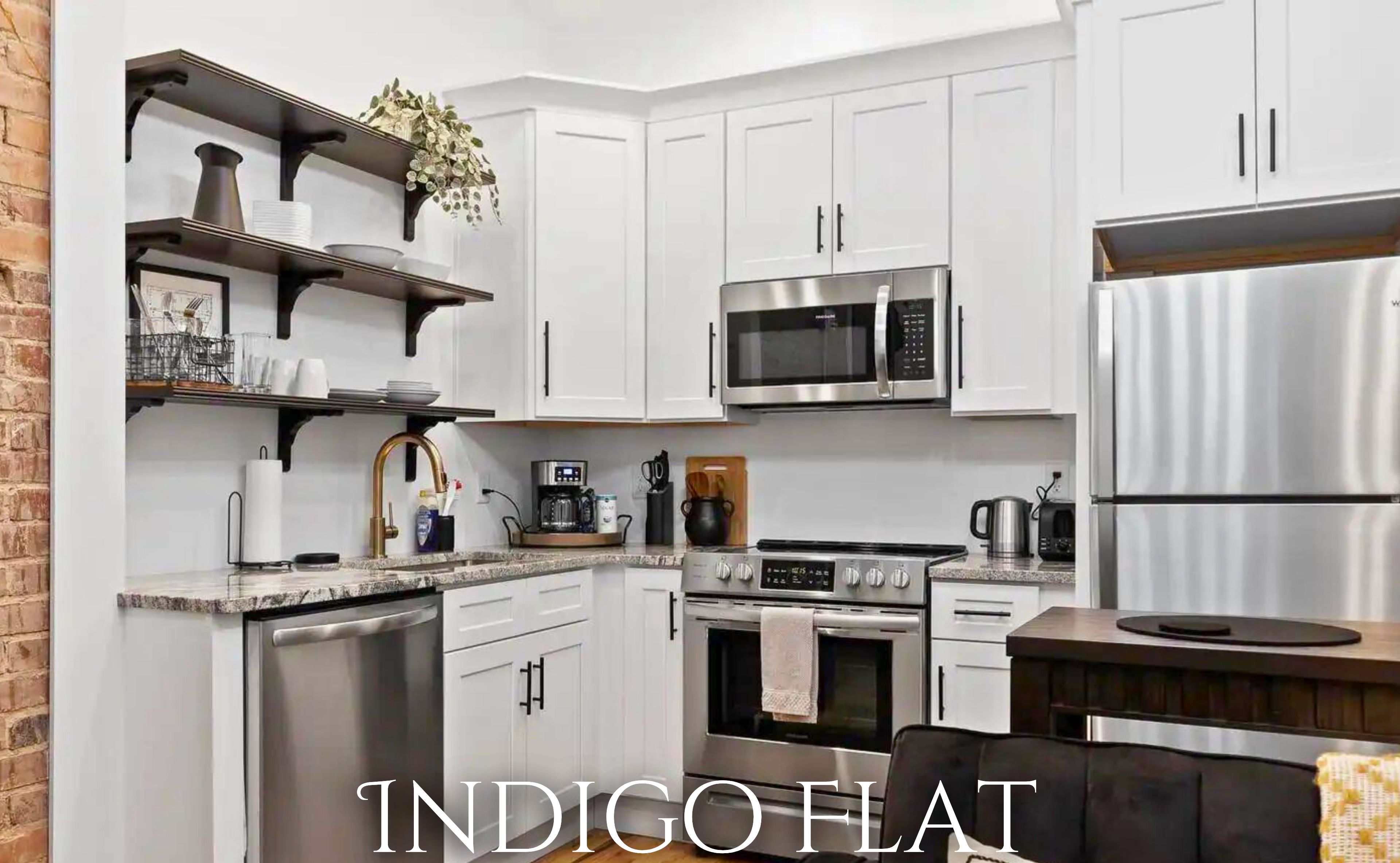 A modern kitchen with white cabinets, stainless steel appliances, and a brick wall.