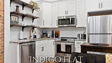 A modern kitchen with white cabinets, stainless steel appliances, and a brick wall.