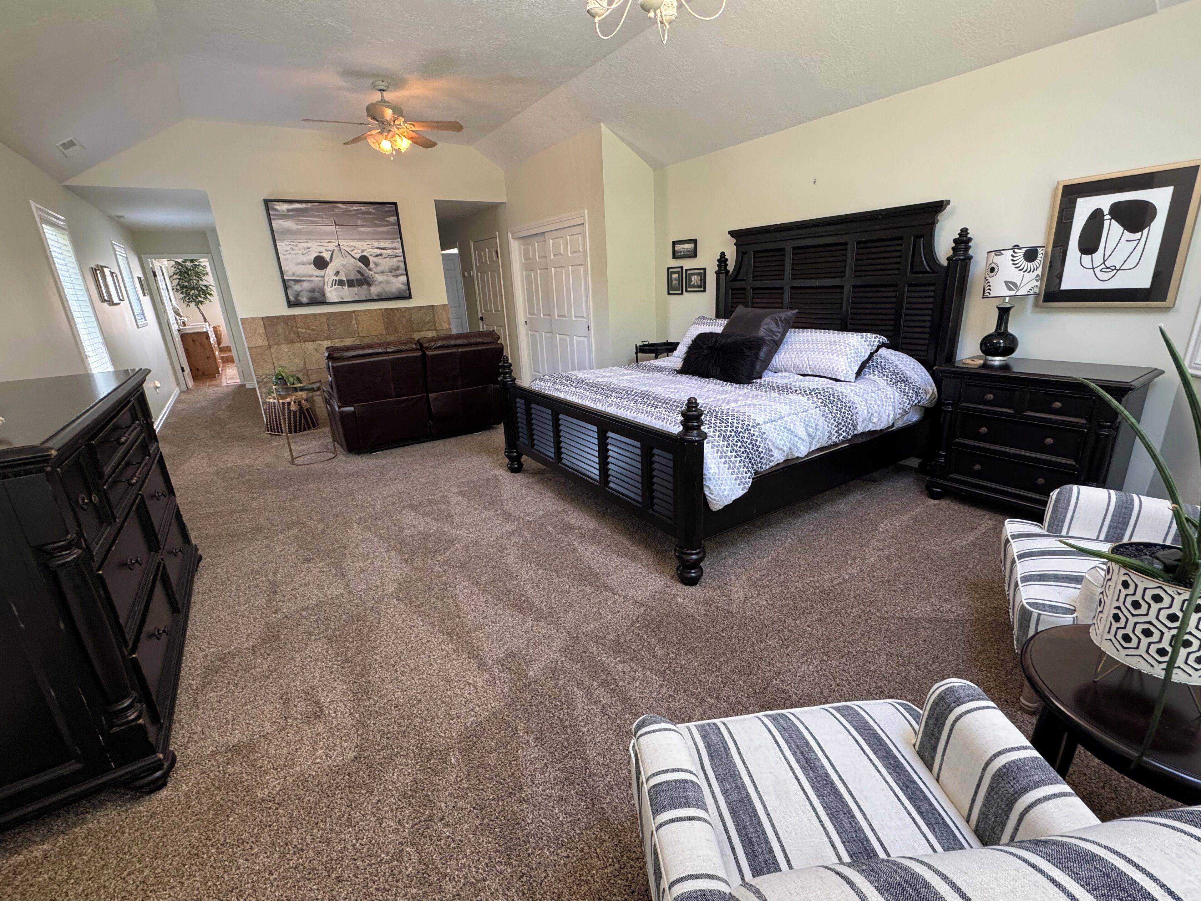Une chambre à coucher avec un grand lit, une commode, une chaise et un ventilateur de plafond.