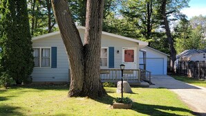 Une maison mobile de plain-pied, dotée d’un porche à l’avant, d’une boîte aux lettres et d’un grand arbre au premier plan.
