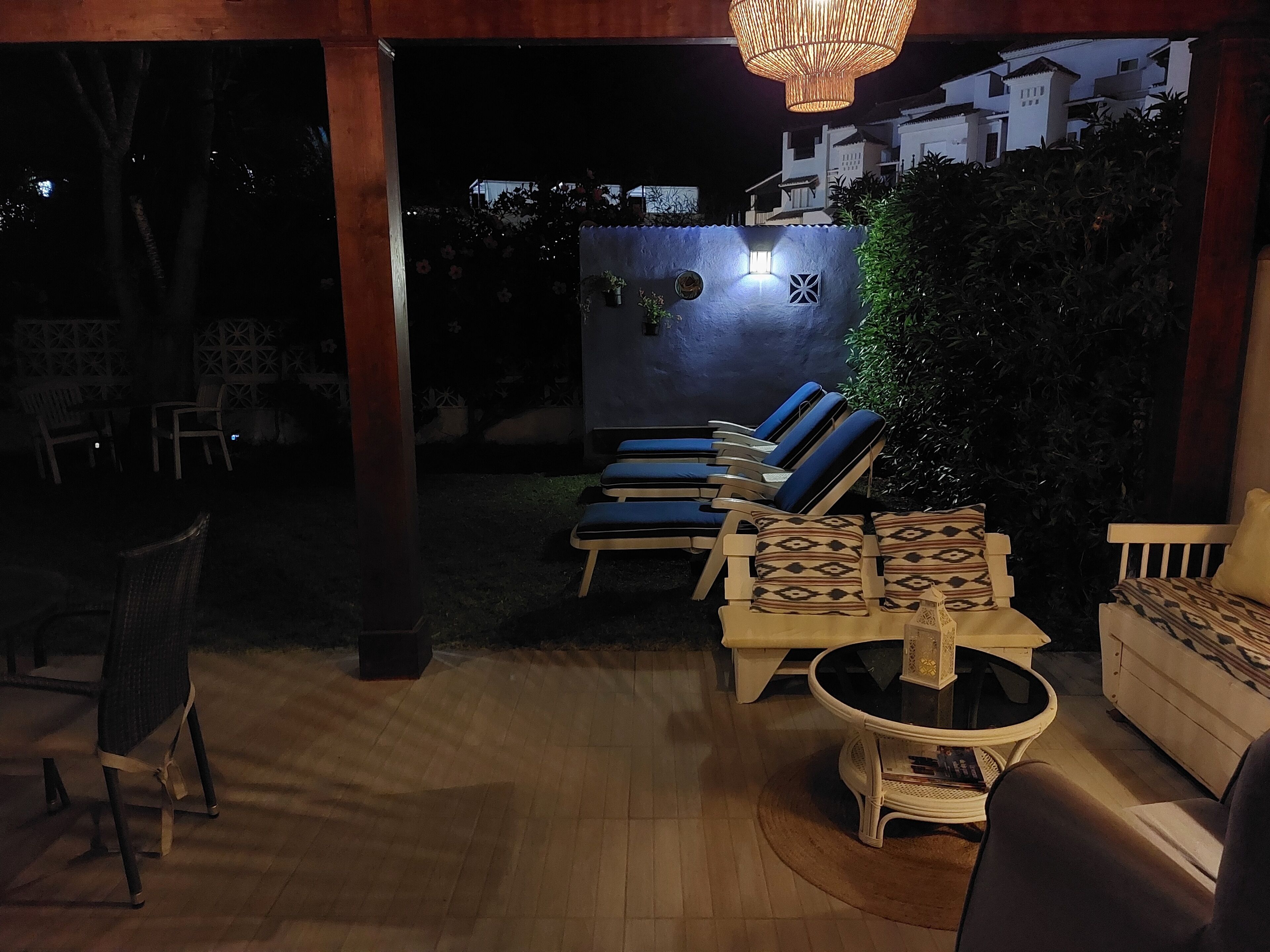 An outdoor seating area with lounge chairs and a table, surrounded by a wooden deck and a wall with a climbing plant.