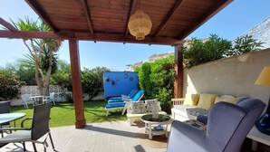 Ein überdachter Patio-Bereich mit Gartenmöbeln, einem Pool und einem Garten.