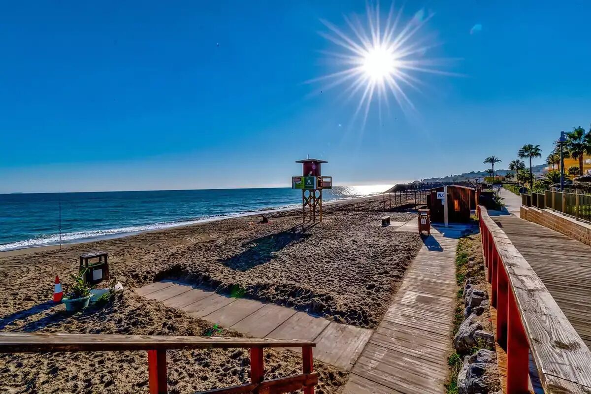 Una playa con una torre de salvavidas, un paseo marítimo de madera y palmeras.
