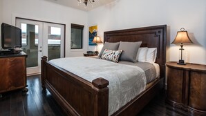 A bedroom with a large bed, wooden headboard, bedside lamps, a TV, and a door leading outside. - Alpenglow Penthouse by Revelstoke Vacations (Revelstoke)
