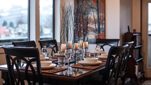A dining table set with plates, glasses, and candles, with a view of a snowy landscape through the window. - Alpenglow Penthouse by Revelstoke Vacations (Revelstoke)