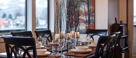 A dining table set with plates, glasses, and candles, with a view of a snowy landscape through the window.