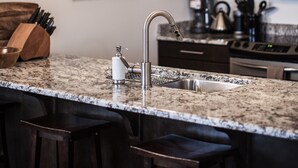 A kitchen with dark wooden cabinets, a granite countertop, a stainless steel sink, and a hanging light fixture. - Alpenglow Penthouse by Revelstoke Vacations (Revelstoke)