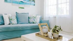 Een woonkamer met een blauwe bank, een witte salontafel en een houten dienblad met decoratieve objecten.
