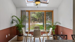 A dining area with a table and chairs, a ceiling fan, and large windows with a view of trees.