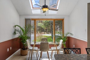 A dining area with a table and chairs, a ceiling fan, and large windows with a view of trees.
