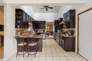 A kitchen with dark cabinets, a central island with bar stools, a ceiling fan, and a view into the dining area.