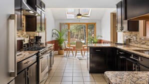A modern kitchen with dark cabinetry, a central island, and a dining area with a view of the forest.