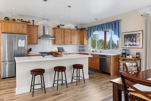 Enjoy cooking in this kitchen with a central island, bar stools, stainless steel appliances, and a large window offering a view of the outdoors.