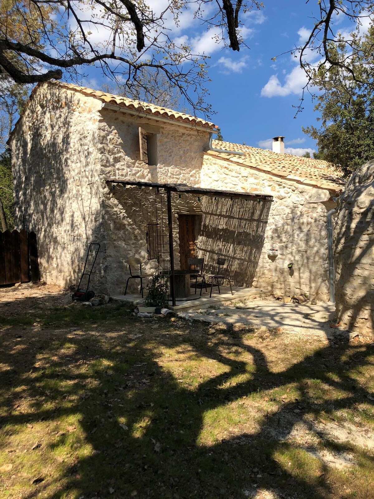 Un bâtiment en pierre avec un toit en tuiles, un patio couvert avec des chaises et une petite table.