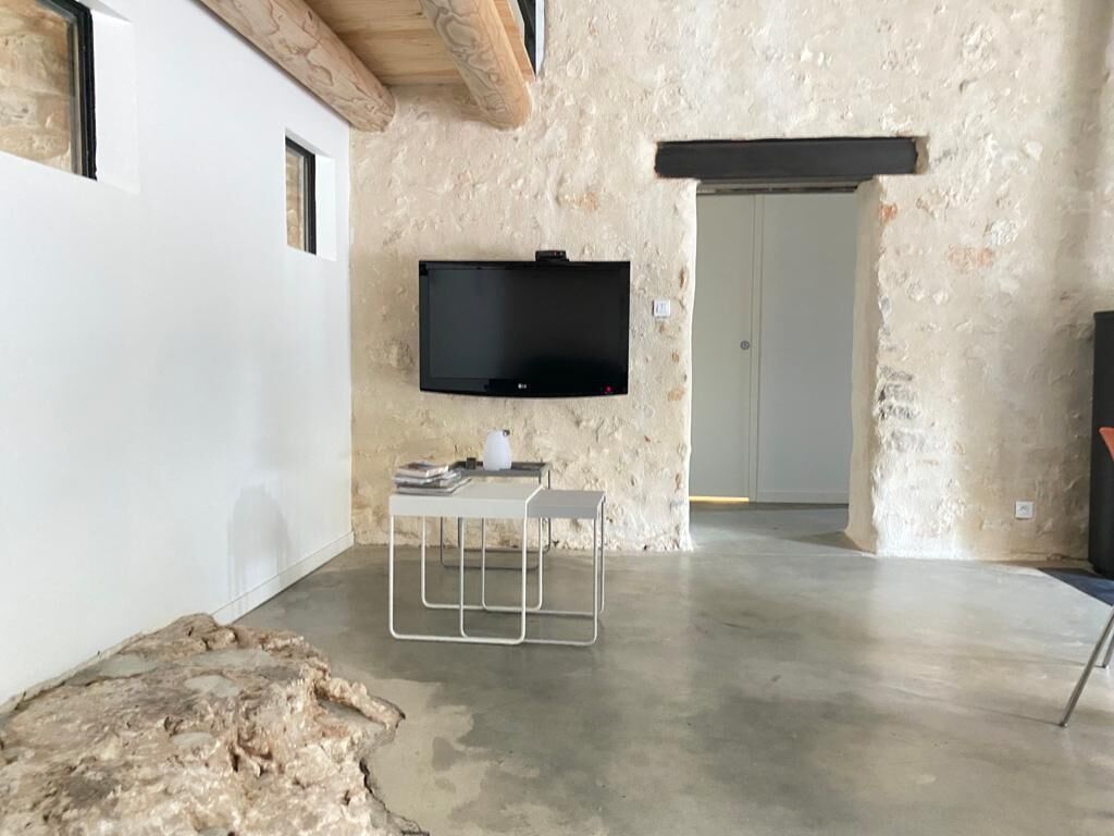 Une pièce avec un mur en pierre, un téléviseur fixé au mur, une table blanche avec un cadre en métal et un sol en béton.