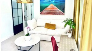 A modern living room with a white sofa, a round coffee table, a potted plant, and a painting of a wooden pier on the wall. - 2 Seasons-4 Bedroom 2 Baths - 2Separate Apartments (Miami)