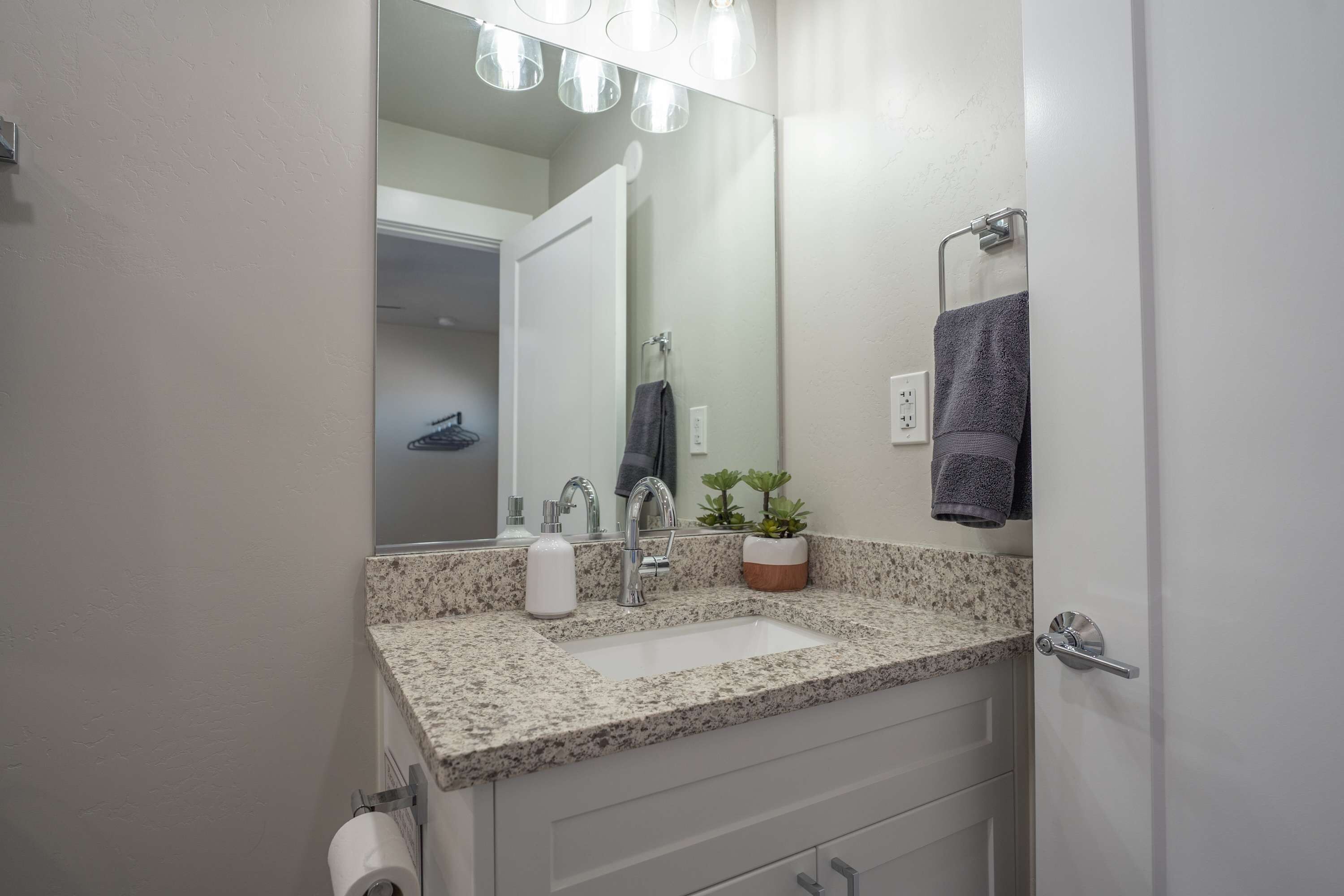 A bathroom with a granite countertop, a sink, a mirror, a towel rack, and a potted plant.