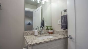 A bathroom with a granite countertop, a sink, a mirror, a towel rack, and a potted plant.