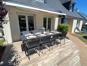 An outdoor patio with a rectangular table set for four, surrounded by chairs, and a small potted plant.