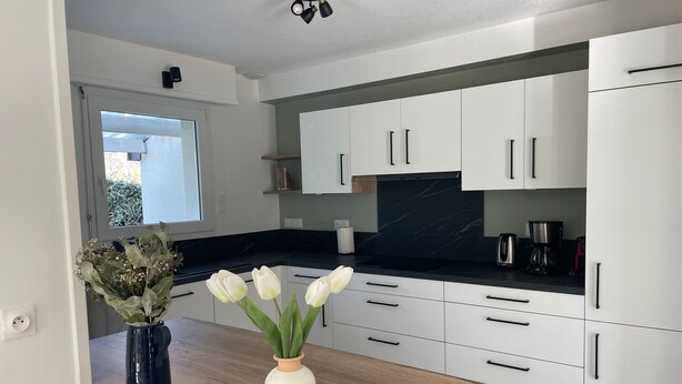Una cocina moderna con armarios blancos, encimera negra y ventana con vistas a zonas verdes.