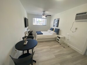 A compact, well-lit room with a bed, a small table, and a ceiling fan.