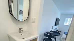 A modern bathroom with a white sink, wooden cabinet, and a large mirror. There is a dining area with a table and chairs in the background. - Excellent location Miami Brickell Studio 1.7 Miles from the Beach (Miami)