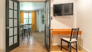 A room with a wooden desk, a chair, a TV mounted on the wall, and a large window with curtains. - Near Red Rocks & Trails • Private Luxury Home (Wheat Ridge)