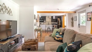 A living room with a television, a sofa with decorative pillows, and a kitchen in the background. - Near Red Rocks & Trails • Private Luxury Home (Wheat Ridge)