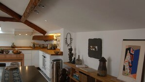 A modern kitchen with wooden beams, a dining area with a patterned rug, and a bookshelf with various items. - 2 room loft Rue de la Croix / Cannes (Cannes)