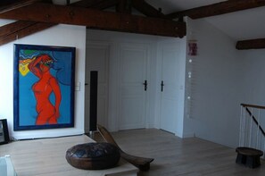 Une pièce avec un plancher en bois, un tableau encadré au mur, un banc en bois et une porte dotée d’un cadre blanc.