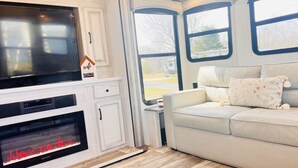 A modern RV interior with a kitchen area featuring a built-in stove, a flat-screen TV, and a WiFi sign. There is a seating area with a sofa and pillows. - Lakefront 1 bedroom tiny home (Acton)
