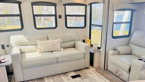 A cozy interior with a sofa and armchair, large windows, and a small table with a candle. - Lakefront 1 bedroom tiny home (Acton)