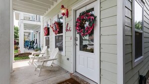Une véranda avec des balustrades blanches, deux fauteuils Adirondack blancs et un paillasson sur lequel est écrit le mot « Sunshine ».