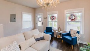 Un salon avec un canapé beige, deux fauteuils bleus, un lustre et deux fenêtres décorées de guirlandes.