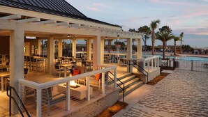 A covered outdoor area with tables and chairs, a pool, and palm trees. - Renovated Oceanview End Unit w/ Use of Hilton Ocean Oak Resort and Amenities (Hilton Head Island)