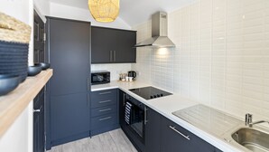 Une cuisine moderne avec des meubles de couleur sombre, un plan de travail blanc, un four encastré et un évier en acier inoxydable.