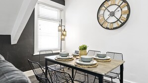 Un coin repas avec une table en bois, des chaises noires et une grande horloge murale.