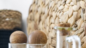 Une planche à découper en bois, un récipient en verre rempli de graines, un verre contenant une substance blanche et une bouteille en verre contenant un liquide jaune.