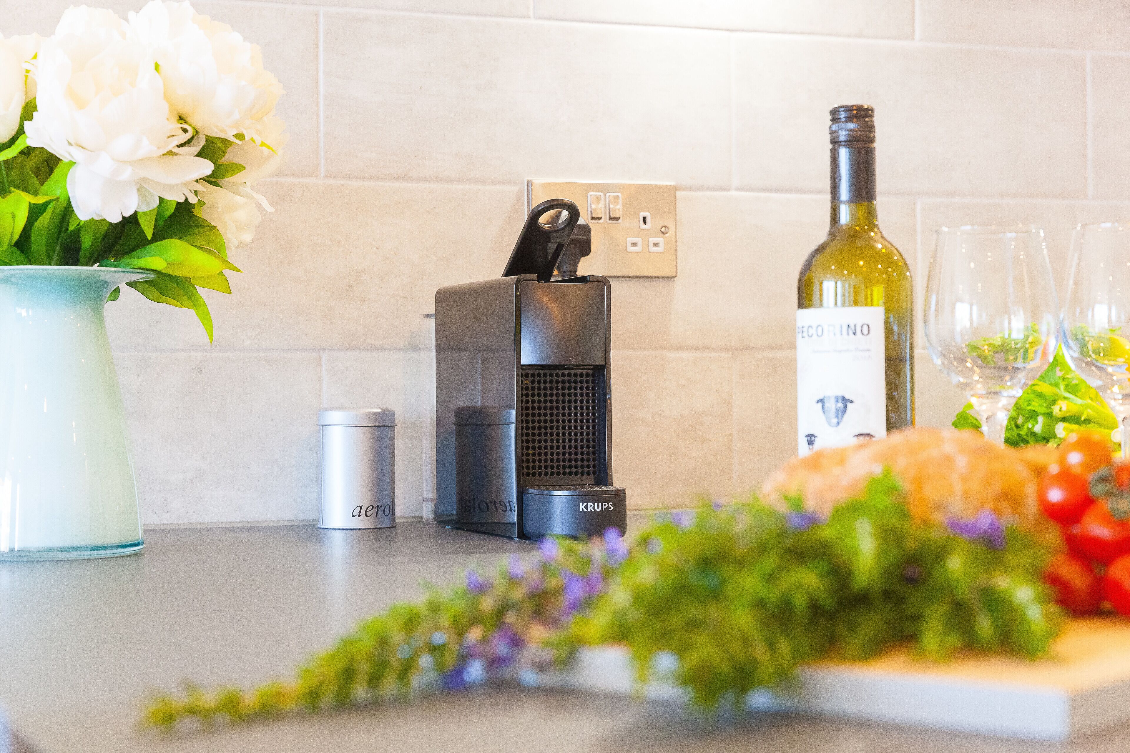 Un comptoir de cuisine orné d’un vase de fleurs, d’une bouteille de vin, d’un haut-parleur et de quelques aliments.
