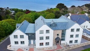A coastal building with multiple white and grey roofs, surrounded by lush greenery and overlooking the sea. - Sea Glass (St Ives)