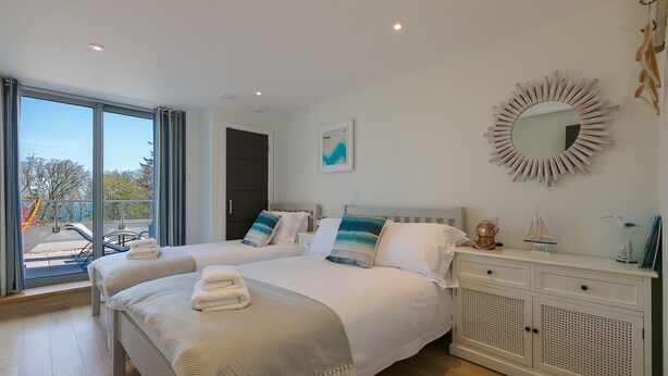 A hotel room with two beds, a large window, a mirror, and a small table with decorative items. - Sea Glass (St Ives)