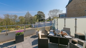 An outdoor patio with wicker furniture, a dining table set, and potted plants. - Sea Glass (St Ives)