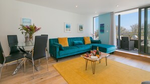 A modern living room with a teal sofa, black chairs, a glass coffee table, and a yellow rug. - Sea Glass (St Ives)