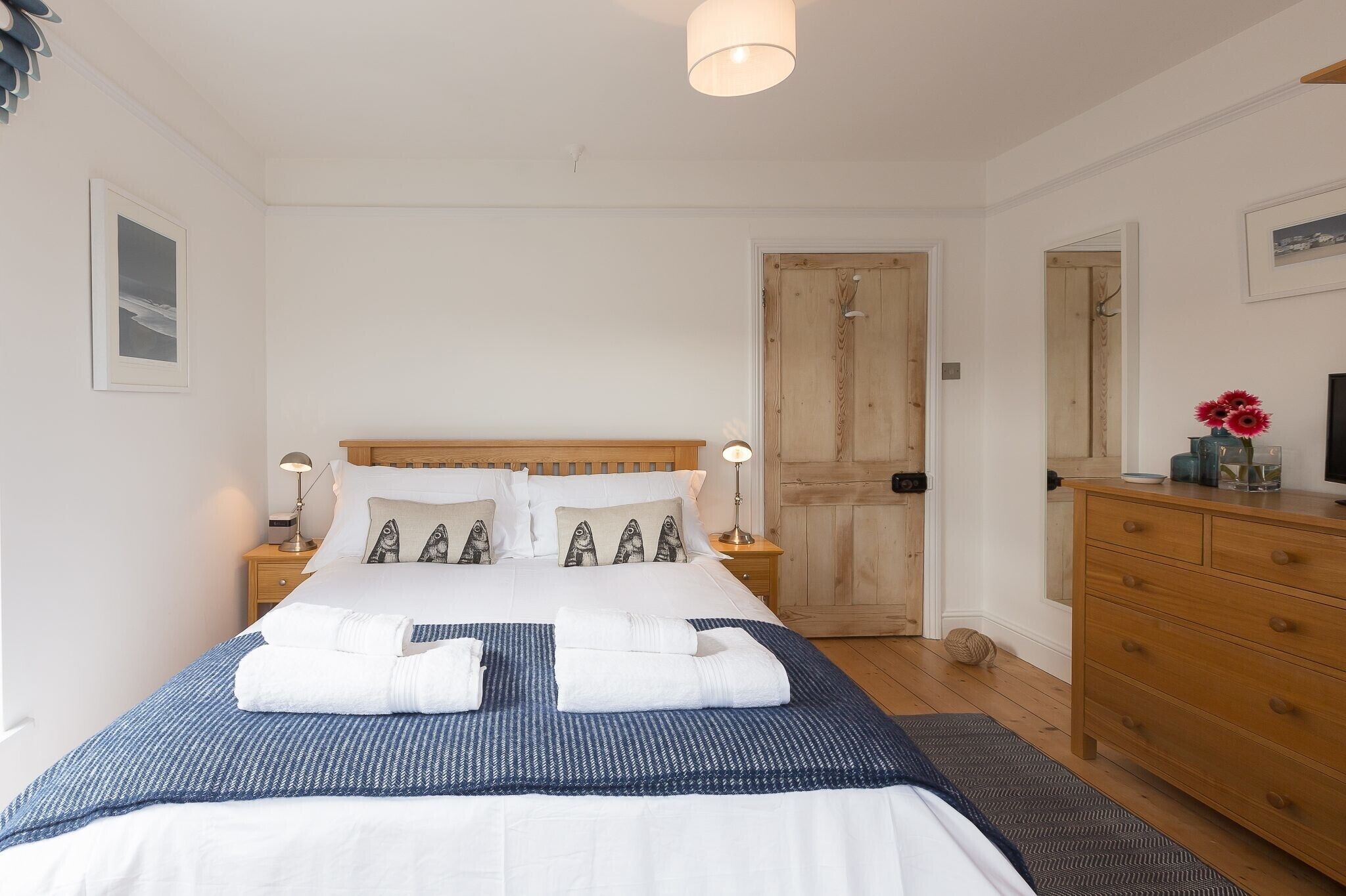 Une chambre à coucher bien rangée, avec un lit, des tables de chevet, une commode et une porte.