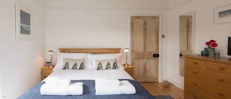 Une chambre à coucher bien rangée, avec un lit, des tables de chevet, une commode et une porte.