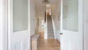 A hallway with a wooden floor, white doors, a bench, and a staircase with a striped railing. - Sea Dream (St Ives)