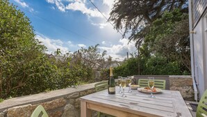 An outdoor dining area with a wooden table, green chairs, and a bottle of wine. - Sea Dream (St Ives)